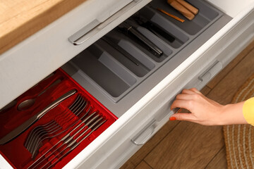 Young woman opening kitchen drawer with cutlery, closeup