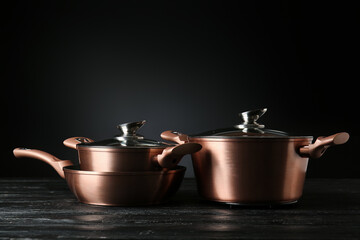 Shiny cooking pots with frying pan on wooden table against dark background