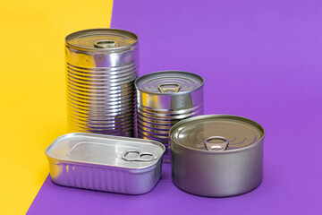 A Group of Stacked Tin Cans with Blank Edges on Split Yellow and Violet Background. Canned Food. Different Aluminum Cans for Safe and Long Term Storage of Food. Steel Sealed Food Storage Containers