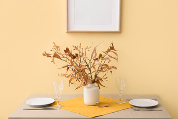 Beautiful table setting and vase with autumn decor near color wall