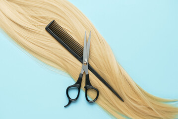 Blonde hair strand for donation with scissors and comb on blue background