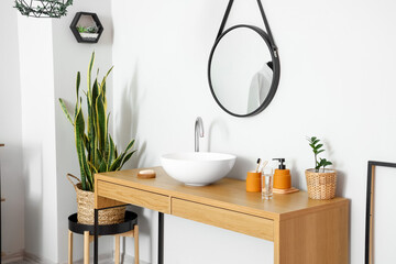 Wooden table with sink and bath supplies near light wall in room