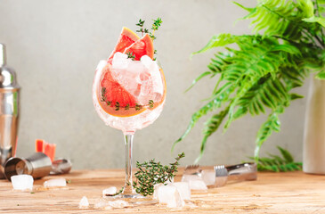 Gin tonic trendy alcoholic cocktail drink with dry gin, bitter tonic, lemon juice, grapefruit, thyme and ice with bar tools. Wooden table background with copy space - obrazy, fototapety, plakaty