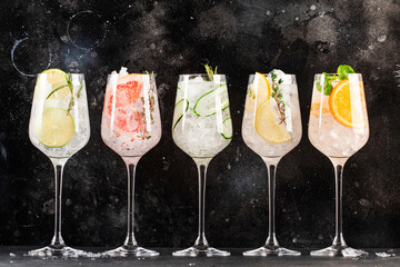 Gin and tonic cocktails set. Trendy Alcoholic drinks with lime, lemon, grapefruit, orange, cucumber, soda and spicy herbs in wine glasses, black background. Summer cocktail party