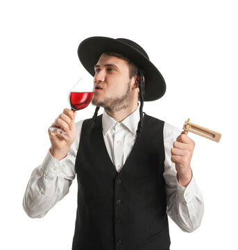 Young Jewish man with glass of wine and gragger for Purim holiday on white background