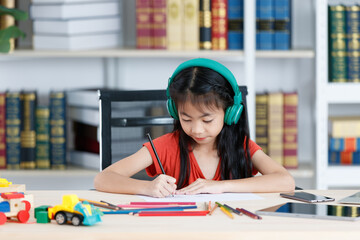 Asian creative young primary school girl artist in casual outfit sitting using color pencil drawing painting picture at home school classroom lesson in living room during pandemic quarantine period