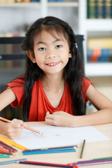 Asian creative young primary school girl artist in casual outfit sitting using color pencil drawing painting picture at home school classroom lesson in living room during pandemic quarantine period
