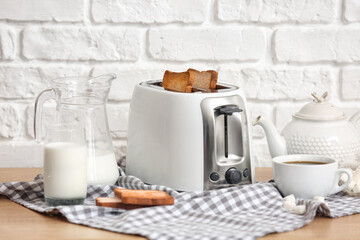 White toaster with bread slices and drinks on table near brick wall