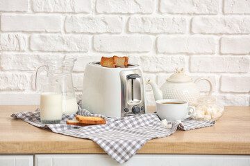 Fototapeta na wymiar White toaster with bread slices and drinks on table near brick wall