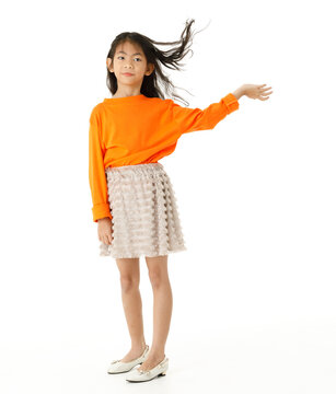 Full body cutout isolated studio shot of Asian young primary schoolgirl model in casual orange shirt and skirt outfit standing holding hand spreading long hair blowing with wind on white background