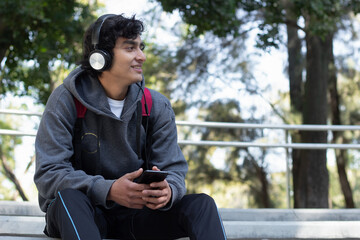 Obraz premium young man enjoying some time alone relaxing listening to music with his headphones in the park, he has a smile on his face and a facial expression of peace and well-being.