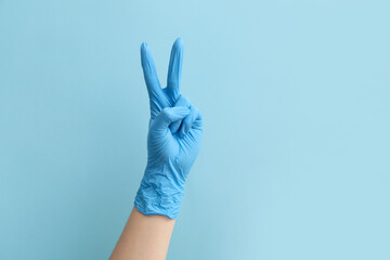 Female doctor in medical glove showing two fingers on blue background