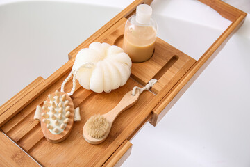 Wooden tray with accessories on white bathtub, closeup