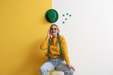 Young woman with decor for St. Patrick's Day sitting in chair on color background