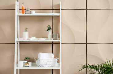 Shelving unit with bath accessories near beige wall