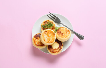 Plate with tasty cottage cheese pancakes on pink background