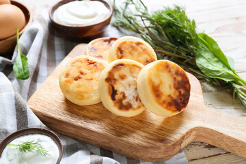 Board with tasty cottage cheese pancakes and sauce on table, closeup