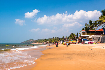 Tourists at tropical, sandy Anjuna Beach on the Goa coast with blue sky, India - obrazy, fototapety, plakaty