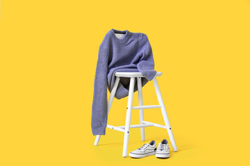 Chair with knitted sweater for child and shoes on color background