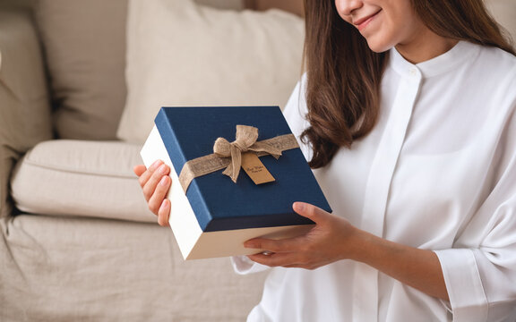 Closeup image of a young woman holding and looking at a present box at home