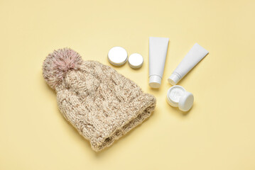 Knitted hat and different cosmetic products on color background