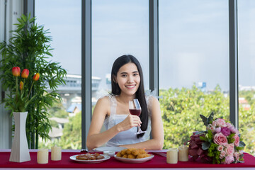 Valentine's day concept, Asian young girl sitting at a table food with wine glasses and bouquet of red and pink roses wine and waiting for her man at in the restaurant background