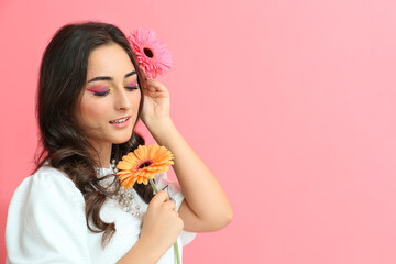 Fototapeta premium Beautiful woman with creative makeup and gerbera flowers on pink background. International Women's Day