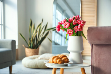 Vase with tulip flowers and plate with croissants on coffee table in living room