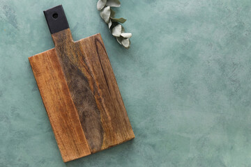 Wooden cutting board and eucalyptus branch on green background