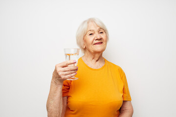 Portrait of an old friendly woman in yellow t-shirts a glass of water in his hands cropped view