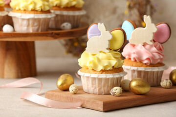 Board with tasty Easter cupcakes and eggs on light table, closeup