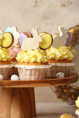 Stand with tasty Easter cupcakes and eggs on light background, closeup