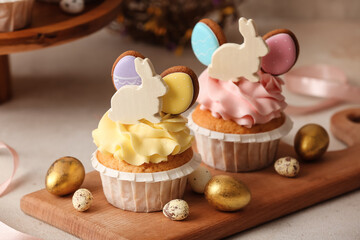 Board with tasty Easter cupcakes and eggs on light table, closeup