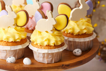 Stand with tasty Easter cupcakes and eggs on light background, closeup