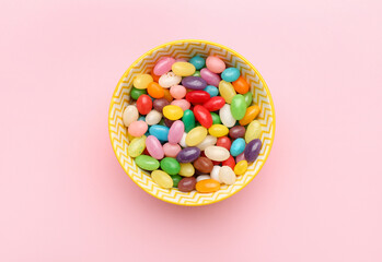 Bowl with multicolored jelly beans on color background