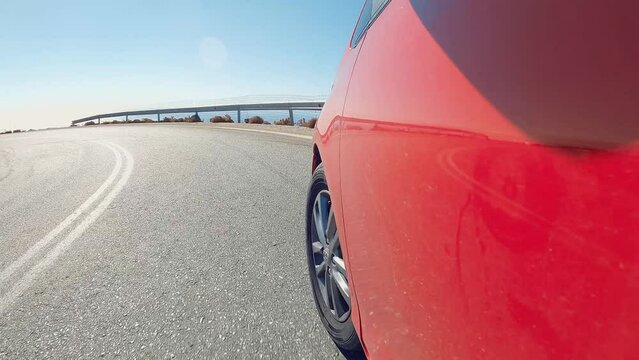 Red car speeds down scenic switchback road running through the idyllic curve mountain road. Sport car drive a challenging serpentine route leading through the stones in Greece. 
