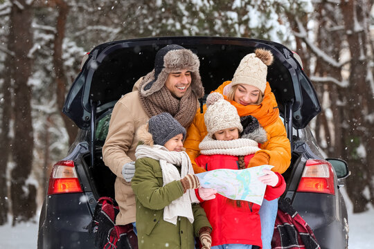 Happy family with map and car in forest on snowy winter day