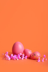 Stylish Easter eggs and flowers on orange background