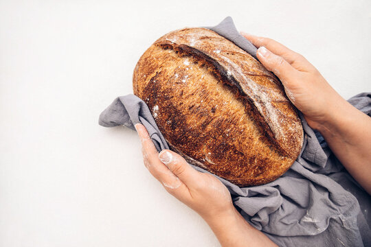 homemade bread in hands. whole grain fresh bread for breakfast. round loaf of bread on a dining white table