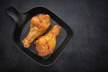 crispy fried chicken drumstick in black skillet pan on the dark tone texture background with copy space for text, top view, flat lay