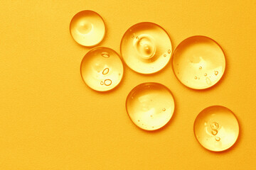 Vitamin serum oil texture. Orange skincare gel drops on bright color background. Gold cosmetic...