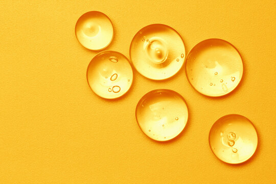 Vitamin serum oil texture. Orange skincare gel drops on bright color background. Gold cosmetic liquid product close up