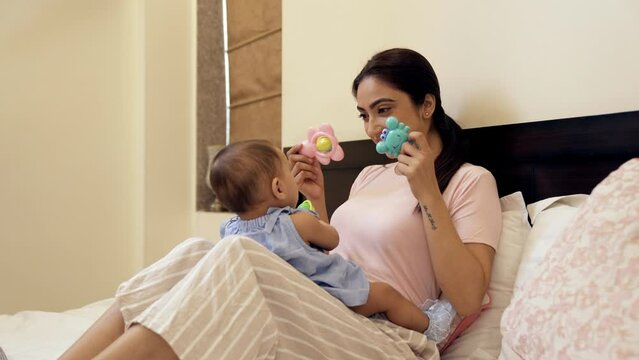 An attractive lady sitting with a cute girl child on her lap at home - baby sitting. A young Indian mother and her pretty little daughter playing with toys - parenting  emotional bonding  nuturing