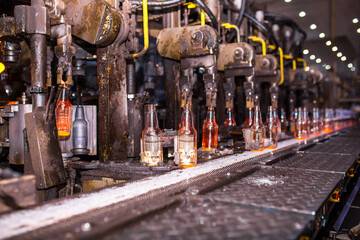 Glass factory, industrial production of glass containers. Modern technology, robots machines make products.Party bottles for drinks. Technological work at the plant. Working atmosphere with copy space