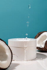 Two halves of coconut and a jar of cosmetics on a blue background with water drops.