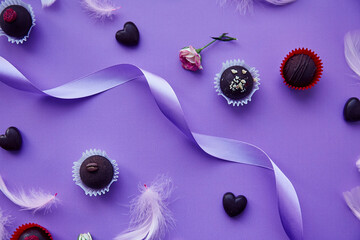 Chocolate and heart shaped sweets. Trendy pink feathers and purple ribbon. Purple pattern. Valentine's Day concept, presents.