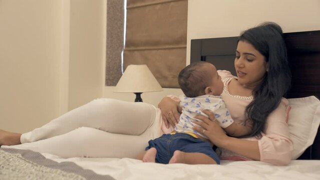 A young mother talking to her newborn baby boy while relaxing at home - parenting  new parent  single mother . Pretty female in a beautiful dress playing with a cute adorable kid in her bedroom - l...