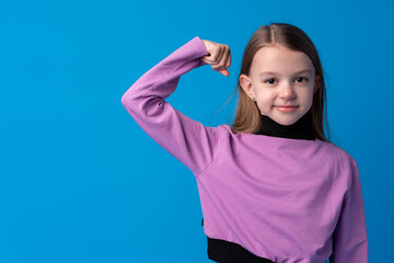 Fototapeta premium Little cute girl showing her strength on blue background
