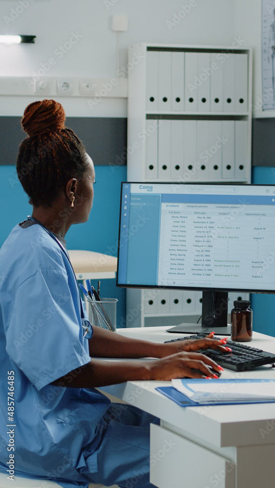 Poster medical assistant typing on computer keyboard in cabinet. woman working as nurse with uniform using 