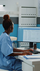 Medical assistant typing on computer keyboard in cabinet. Woman working as nurse with uniform using...
